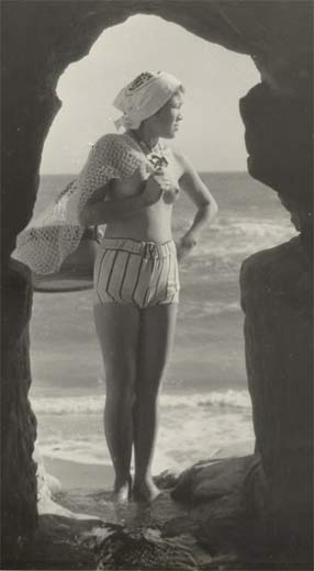 Photographic image of an Ama shellfish diver framed in the entrance to a cave. Her naked breasts are visible.